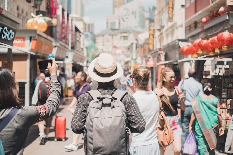 turistas con mochilas recorren una vibrante calle comercial tradicional decorada con faroles rojos.