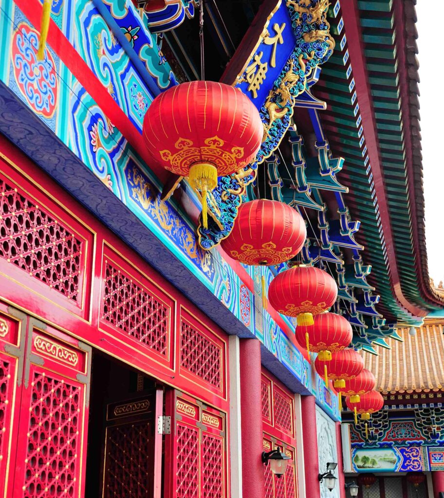 Detalle en primer plano de la colorida fachada de un templo tradicional Chino, adornado con una hilera de faroles rojos colgantes.